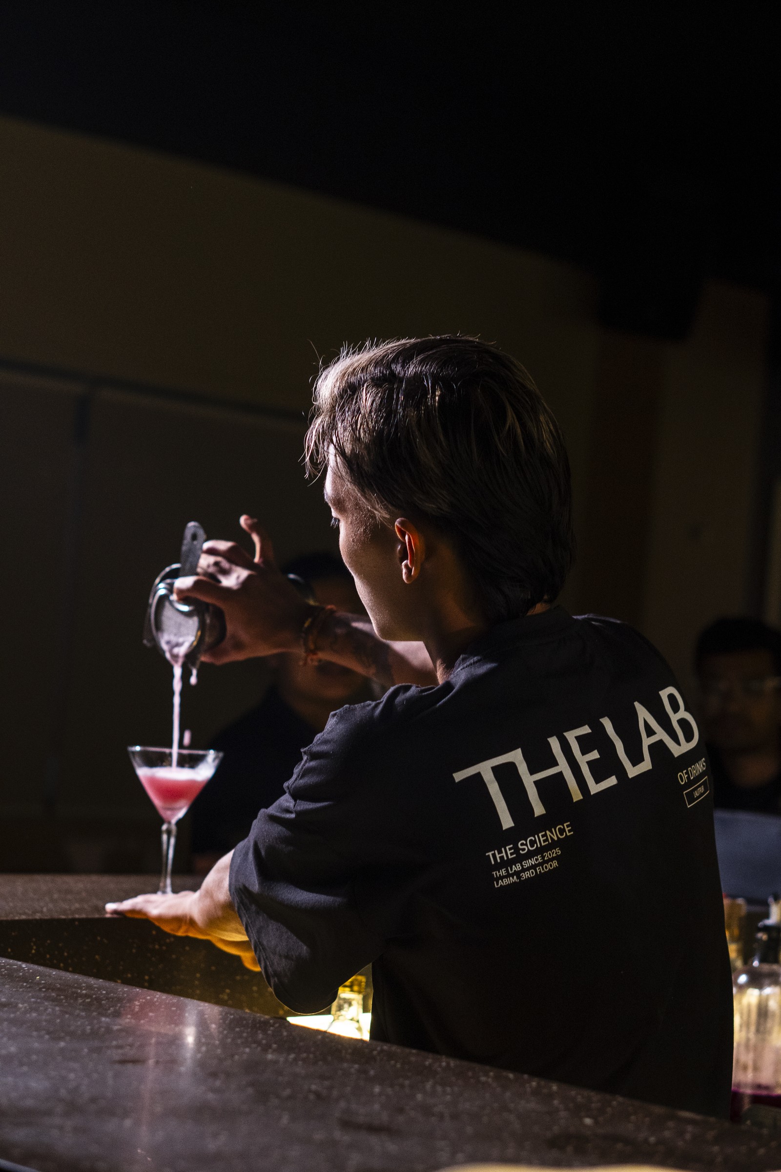 A bartender in The Lab uniform pouring a cocktail